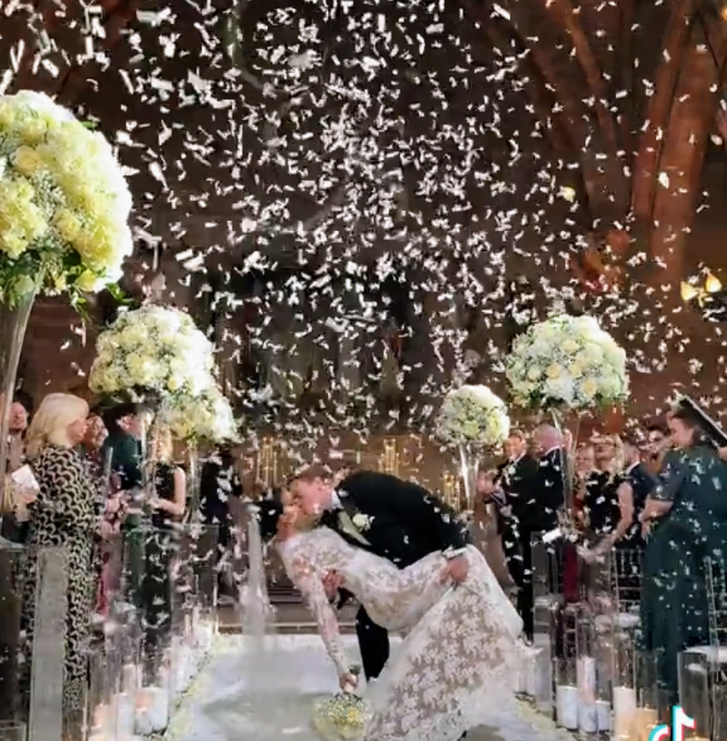 Confetti bursts as a couple shares a romantic kiss, surrounded by white wedding confetti from a confetti cannon