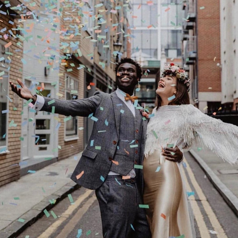 Couple celebrating under a burst of multicolour confetti from a confetti cannon.