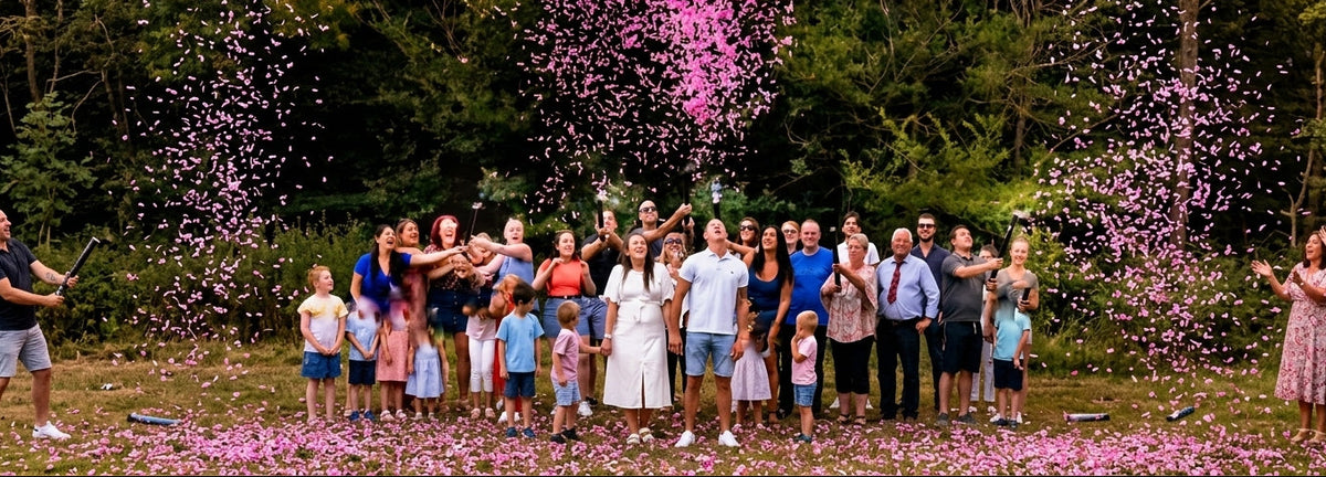 Family at outdoor gender reveal party celebrating with pink confetti cannons, creating a shower of pink confetti.
